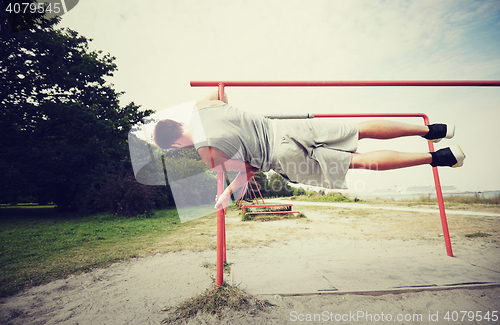 Image of young man exercising on parallel bars outdoors