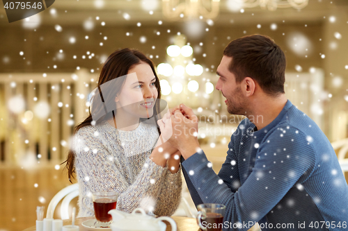 Image of happy couple with tea holding hands at restaurant