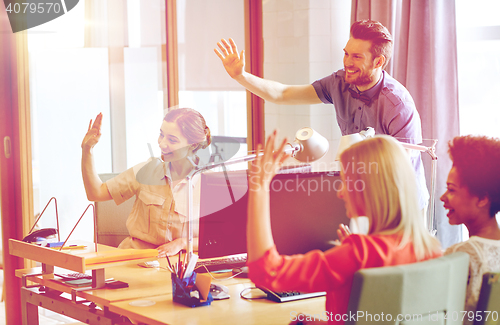 Image of happy creative team waving hands in office
