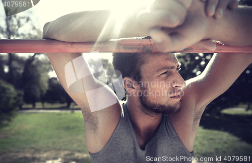 Image of young man exercising on horizontal bar outdoors