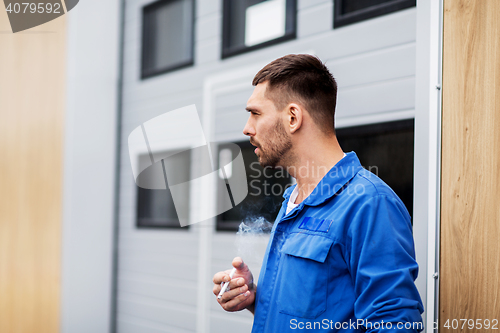 Image of auto mechanic smoking cigarette at car workshop