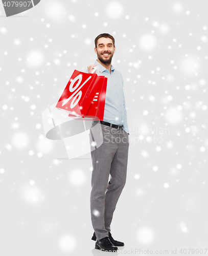 Image of smiling man with red shopping bag over snow