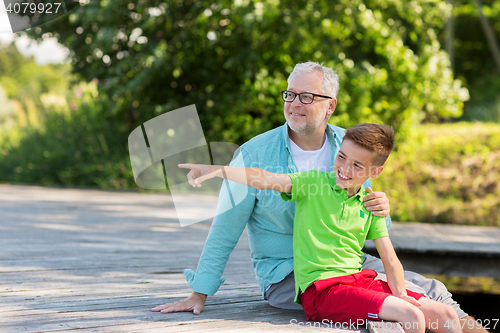 Image of grandfather and grandson sitting on river berth