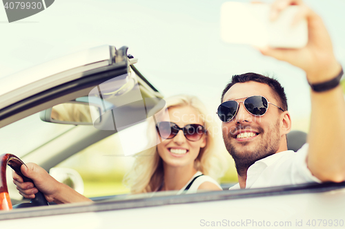 Image of happy couple in car taking selfie with smartphone
