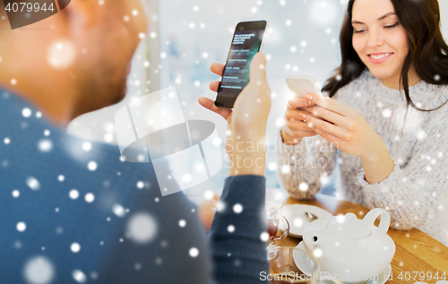 Image of happy couple with smartphones drinking tea at cafe