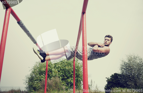 Image of young man doing sit up on parallel bars outdoors