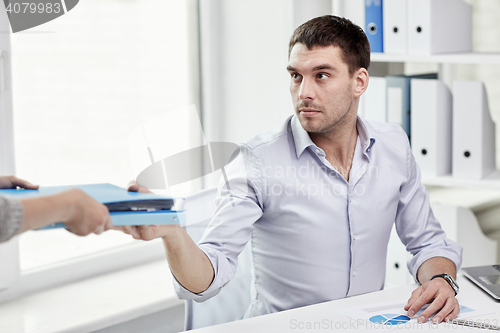 Image of businessman taking folder from secretary in office