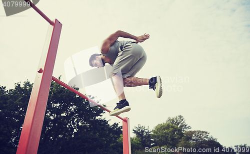 Image of young man jumping on horizontal bar outdoors