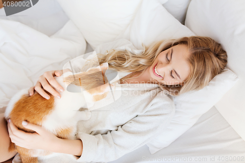 Image of happy young woman with cat in bed at home