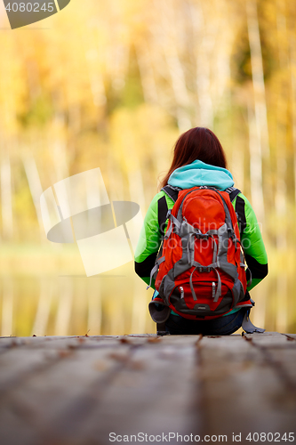 Image of Brunette sitting back with backpack on bridge near water