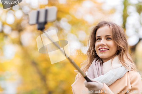 Image of woman taking selfie by smartphone in autumn park