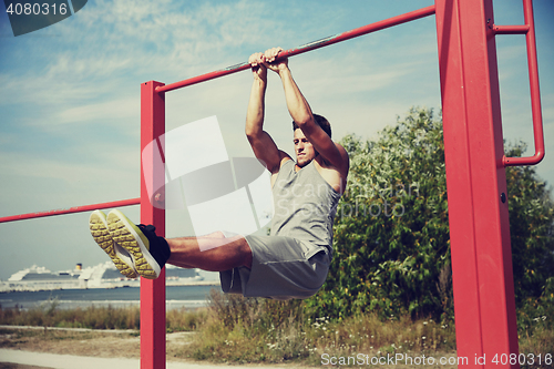 Image of young man exercising on horizontal bar outdoors