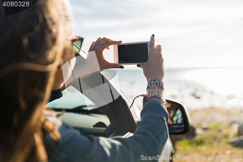 Image of happy young woman in car with smartphone at sea