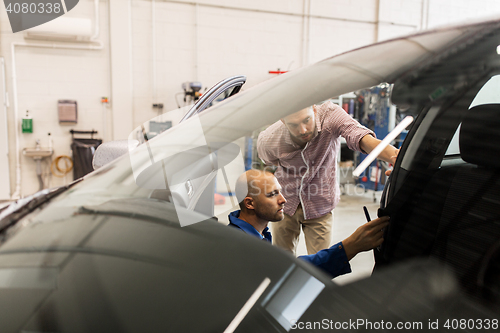 Image of mechanic and man checking seat belt at car shop