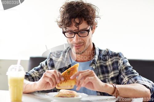 Image of happy man eating sandwich at cafe for lunch