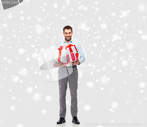 Image of happy young man holding christmas gifts over snow