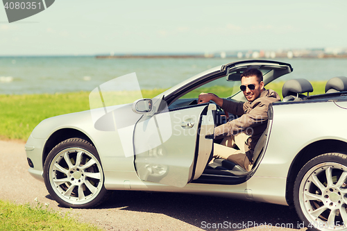 Image of happy man opening door of cabriolet car outdoors