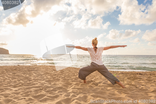 Image of Woman practicing yoga on sea beach at sunset.