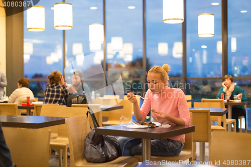 Image of Young woman eating pizza at airport restaurant while waiting for flight departure.