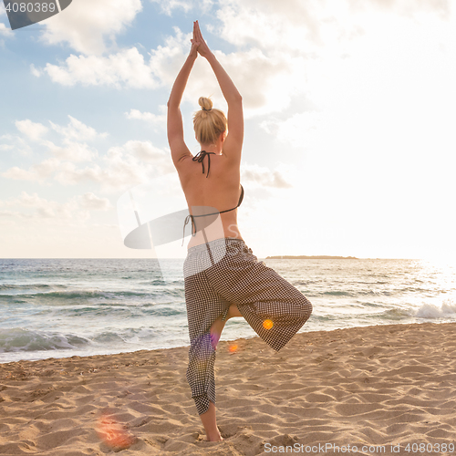 Image of Woman practicing yoga on sea beach at sunset.