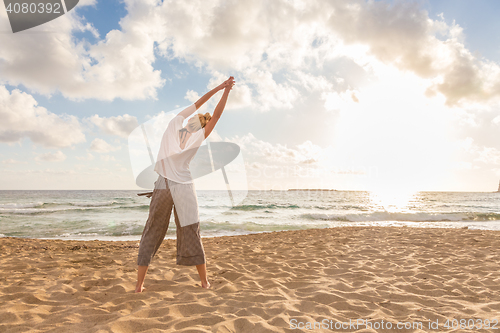 Image of Woman practicing yoga on sea beach at sunset.