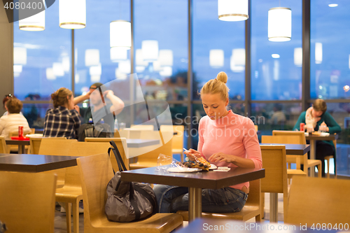 Image of Young woman eating pizza at airport restaurant while waiting for flight departure.