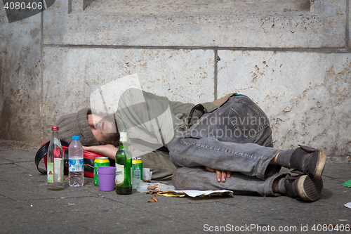 Image of Homeless young alcohol addict lying drunk on street sidewalk in Berlin.