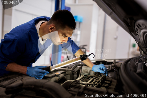 Image of mechanic man with lamp repairing car at workshop