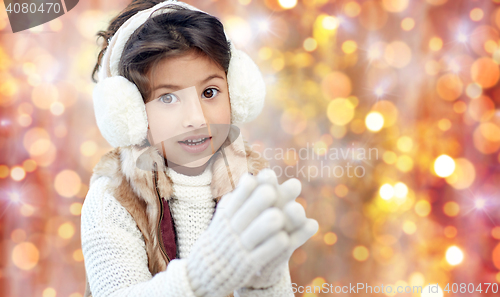 Image of happy little girl in earmuffs over holidays lights