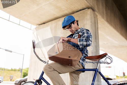 Image of hipster man with bicycle looking something in bag
