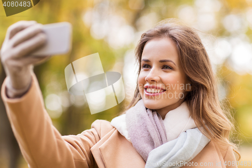 Image of woman taking selfie by smartphone in autumn park