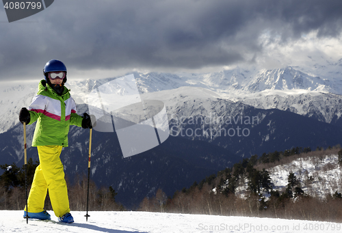 Image of Young skier with ski poles in sun mountains and cloudy gray sky