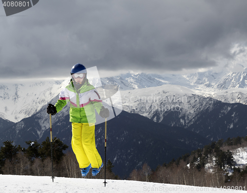Image of Young skier jumping with ski poles in sun mountains and cloudy g