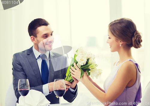 Image of smiling man giving flower bouquet at restaurant