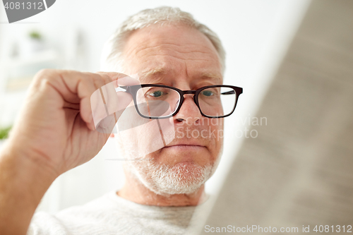 Image of close up of old man in glasses reading newspaper 