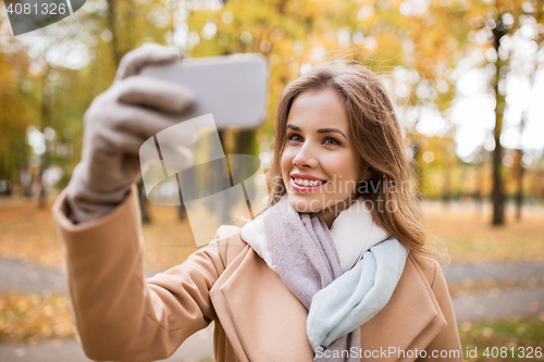 Image of woman taking selfie by smartphone in autumn park