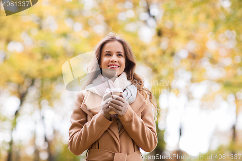 Image of happy young woman drinking coffee in autumn park