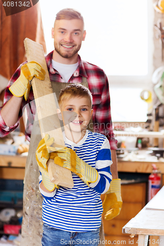 Image of happy father and son with wood plank at workshop