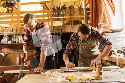 Image of carpenters working with saw and wood at workshop