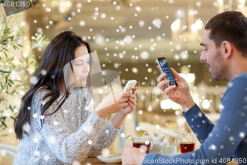 Image of happy couple with smartphones drinking tea at cafe