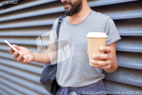 Image of man with coffee texting on smartphone in city