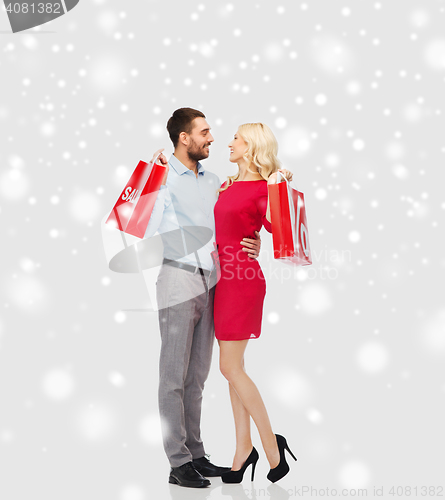 Image of happy couple with red shopping bags over snow