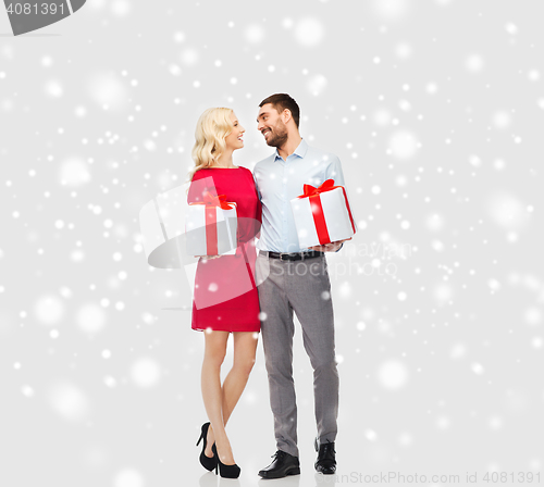 Image of happy couple with christmas gift boxes over snow