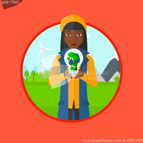 Image of Woman holding light bulb with tree inside.