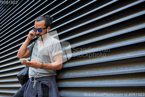 Image of man with earphones and smartphone on city street