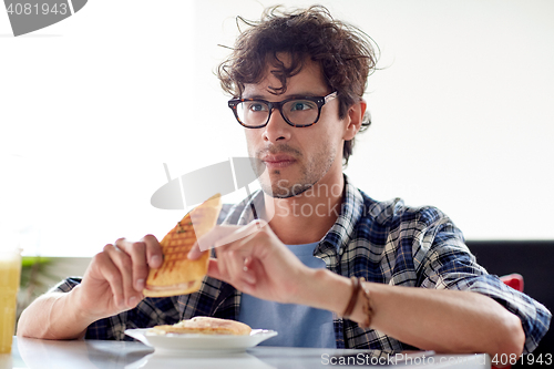 Image of happy man eating sandwich at cafe for lunch