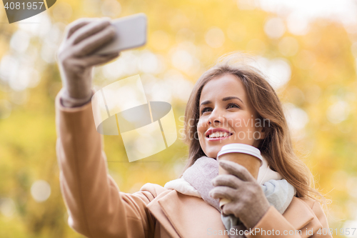 Image of woman taking selfie by smartphone in autumn park