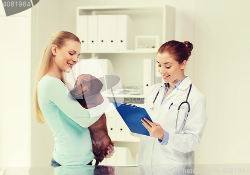 Image of happy woman with dog and doctor at vet clinic