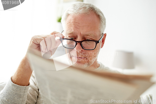 Image of senior man in glasses reading newspaper at home