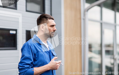 Image of auto mechanic smoking cigarette at car workshop